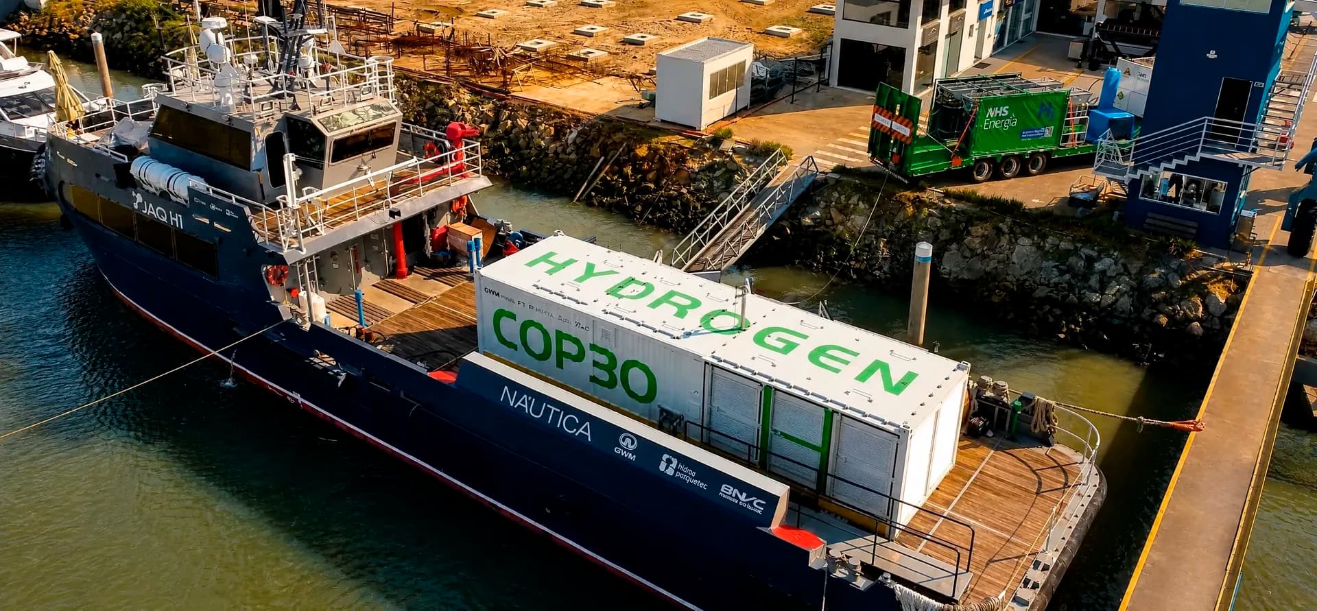 Vista aérea do JAQ H1 atracado na Marina de Itajaí, com o contêiner "Hydrogen COP30" a bordo e a unidade móvel de abastecimento da AHS Energia na doca ao lado